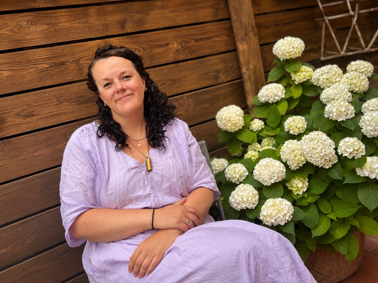 Anne Hühnlein sitzt lächelnd neben blühenden Hortensien