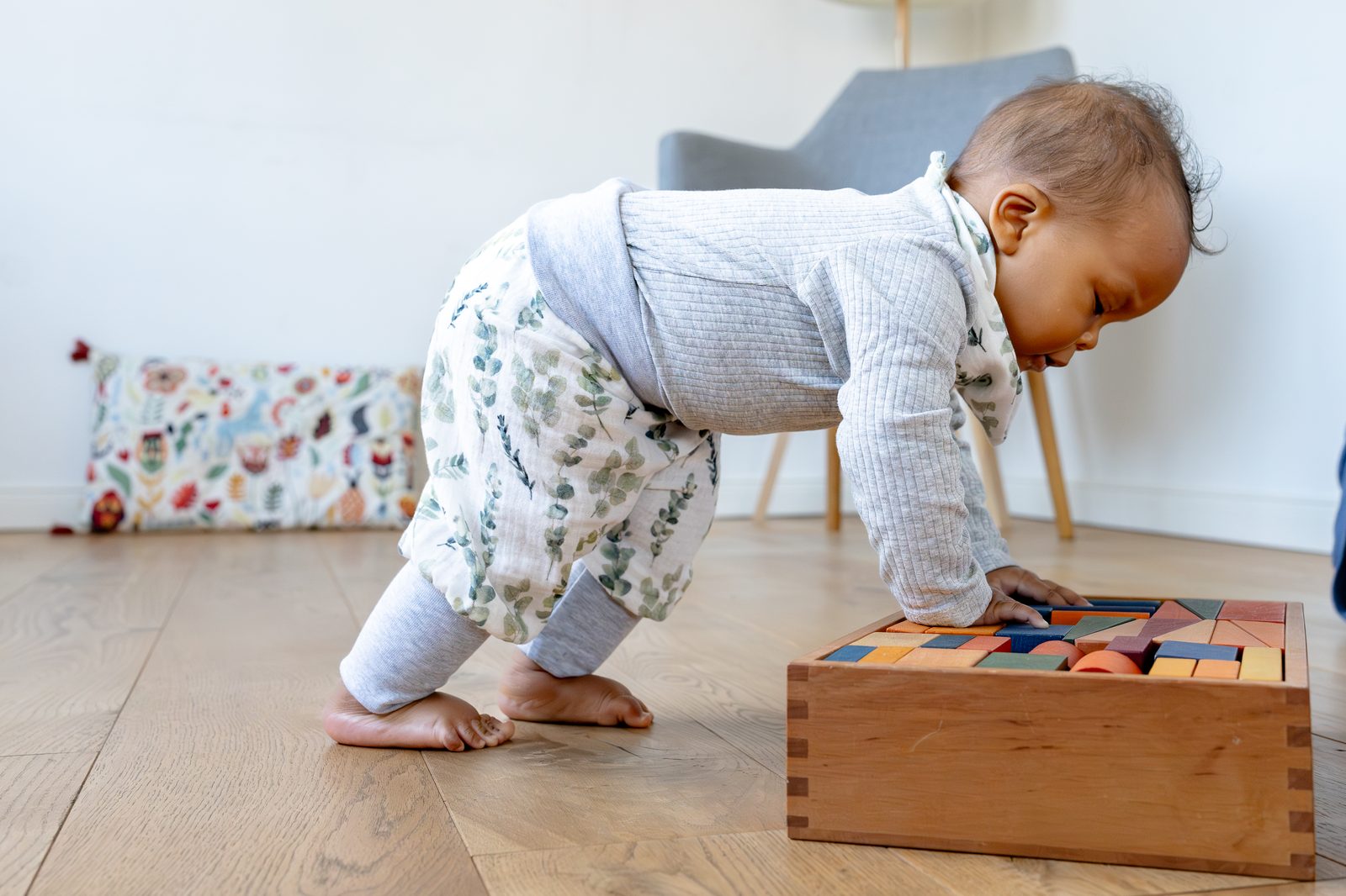 Baby steht gestützt an einer Holzkiste und greift nach Bauklötzen